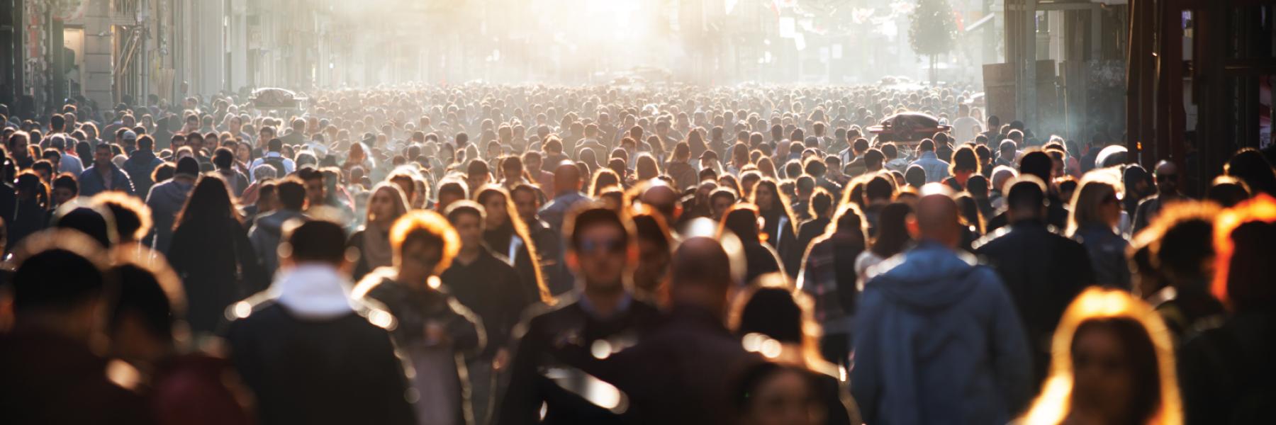 Image of a large crowd of people walking outside in a city block setting