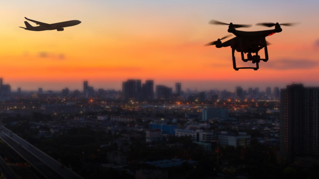 Drone and airplane fly above city skyline at sunset