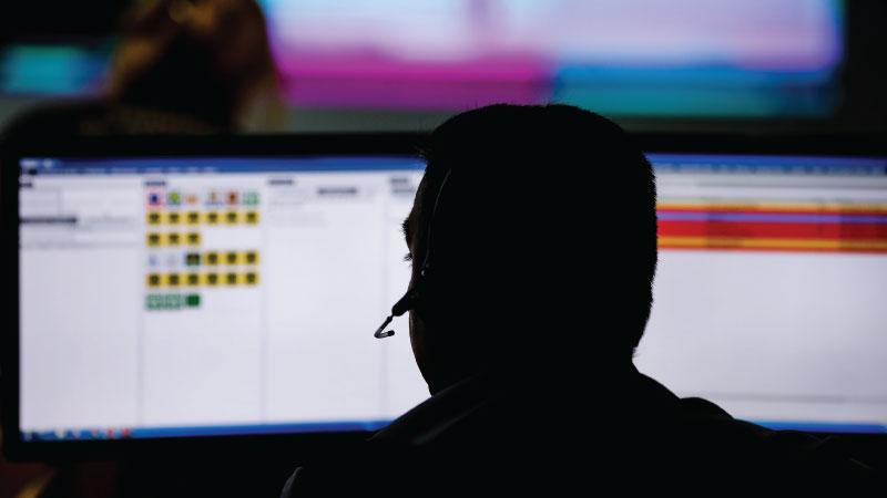 Silhouette of person wearing headset looking at computer monitors 