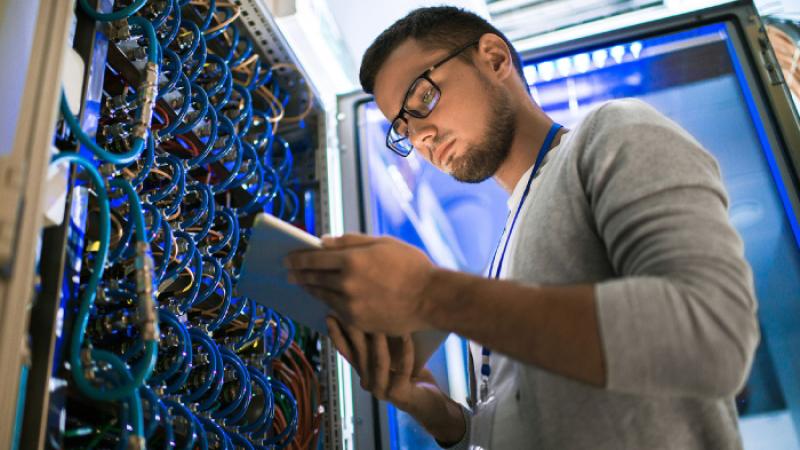 Man standing in front of an open server reviewing data on a device