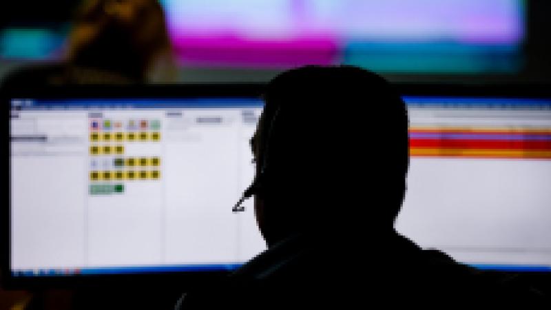 Silhouette of a man with a headset sitting in front of two computer screens