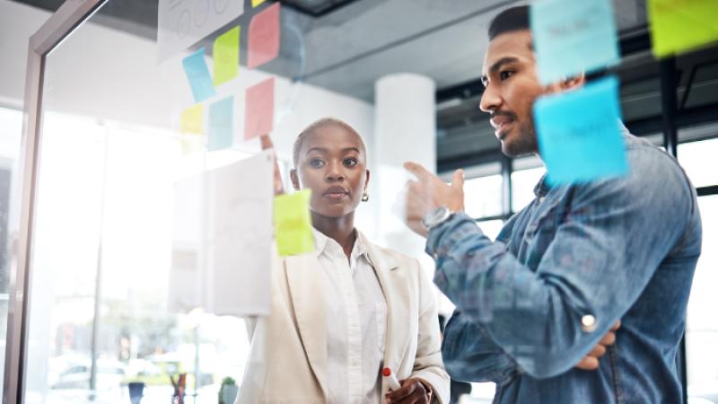 Two individuals discussing behind a glass screen covered in post-it notes