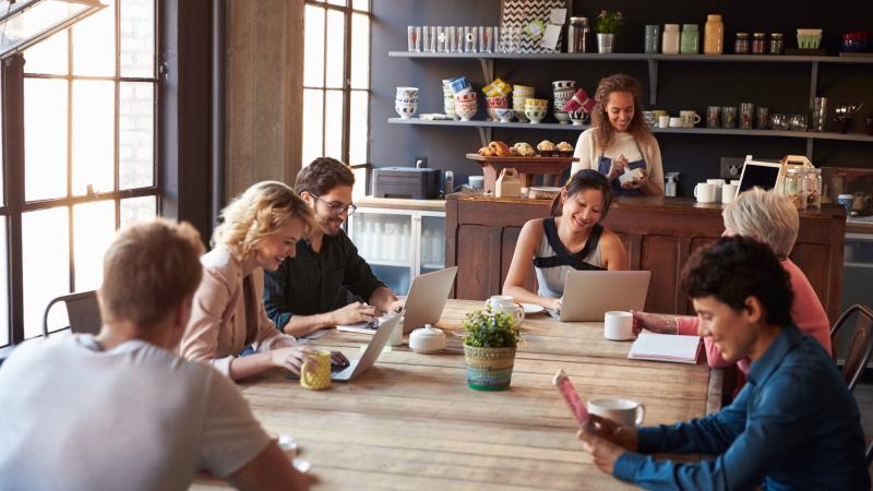 An image of a coffee shop owner and patrons sitting at a table. 