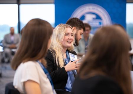 Female CISA intern speaking with other mostly female interns in background.