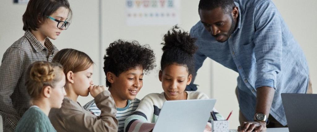 Young students on a computer with their teacher watching and guiding them