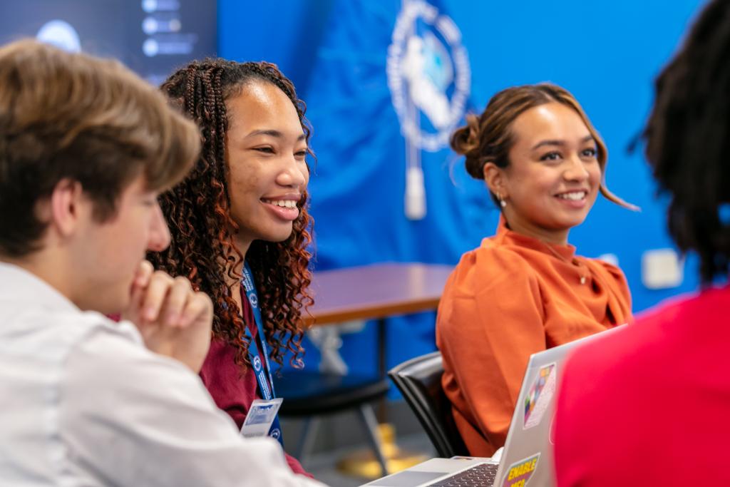 Four diverse interns (2 female, 2 male) in a conference room talking and smiling.