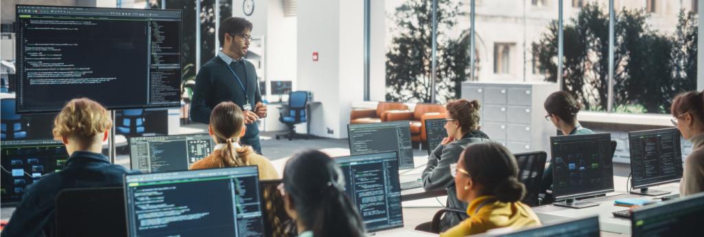 A professor teaching cybersecurity in a computer lab to a diverse group of students.